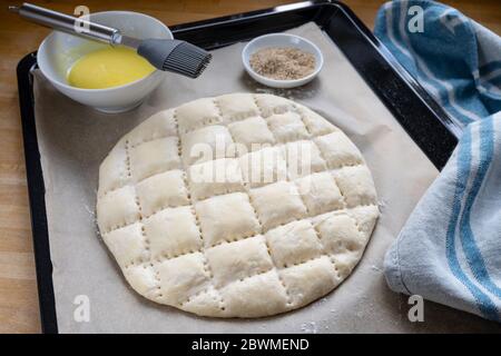 Flacher Brotteig mit dem typischen Muster für türkischen Ramadan-Pide auf einem Backblech mit Papier, Eigelb zum Beschichten und Sesam, ausgewählter Fokus, Stockfoto