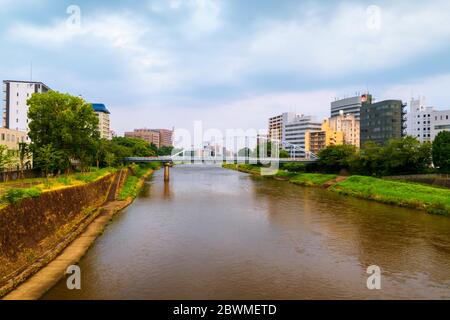 Kumamoto, Japan. Blick auf eine Brücke über den Shirakawa Fluss in Kumamoto, Japan Tagsüber mit Wolkenkratzern Stockfoto