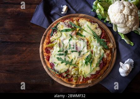 Pizza mit Kruste aus zerfetztem Blumenkohl auf einem dunklen rustikalen Holztisch, Alternative für kohlenhydratarme oder ketogene Ernährung, Kopierraum, Draufsicht von abov Stockfoto