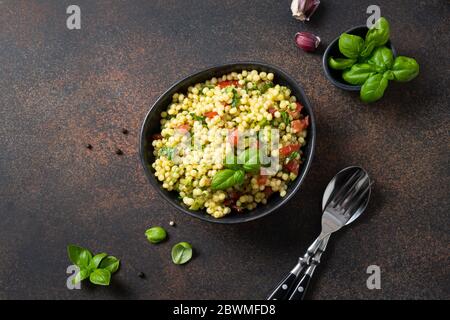 Gemüsesalat mit Pasta Ptitim oder Birdy, israelisch Couscous dekoriert Basilikumblätter auf dunkelbraunem Hintergrund. Draufsicht. Stockfoto