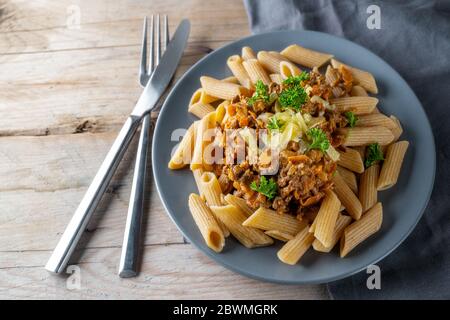 Penne-Vollkornnudeln mit einer Sauce aus Hackfleisch und Karotten, Parmesan-Käse und Petersilie garnieren, Besteck auf einem rustikalen Holztisch, kopieren Raum, se Stockfoto