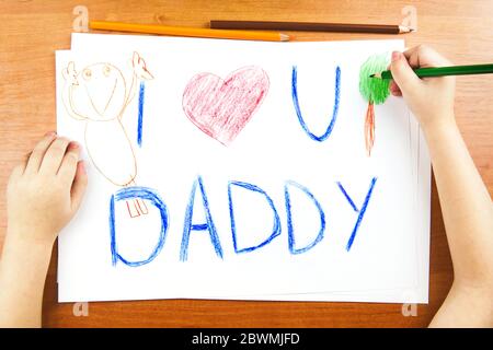 Das Konzept des Vatertags. Childs Hände Zeichnung Karte mit Worten I Love U Papa, und rotes Herz, und Farbstifte auf Holztisch. Stockfoto