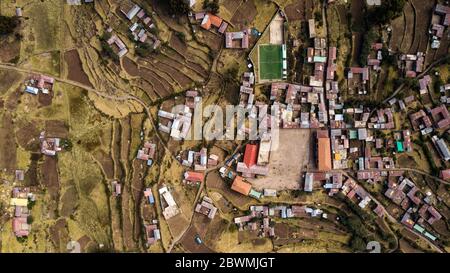 Luftaufnahme von oben auf den Hauptplatz auf der Insel Taquile, sichtbare Häuser, Fußballplatz, terrassierte Pisten, landwirtschaftliche Felder. Titicacasee, Peru. Stockfoto