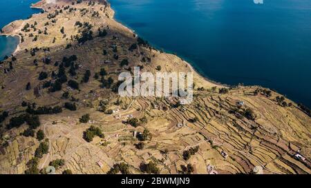 Luftaufnahme auf terrassenförmig angelegten Hängen der Insel Taquile am Titicaca See mit Blick auf blaues Wasser und Sonnenlicht, sichtbare Häuser und Bäume auf der Insel Stockfoto