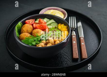 Vegetarische buddha-Schale mit Gurke, Avocado, Falafel, Tomaten und Kichererbsen auf schwarzem Hintergrund Stockfoto