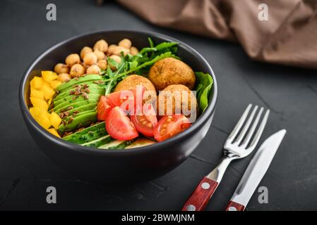 Vegetarische buddha-Schale mit Gurke, Avocado, Falafel, Tomaten und Kichererbsen auf schwarzem Hintergrund Stockfoto