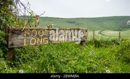 Ein Schild, das zum Long man bei Wilmington auf den South Downs von East Sussex führt, mit der alten Bergfigur in der Ferne. Stockfoto