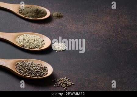 Bio getrocknete Hanfsamen, Mehl, Kerne in drei Holzlöffel auf braunem Hintergrund. Nahaufnahme. Gesunde Zutaten für saubere Ernährung und vegan. Stockfoto