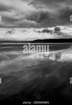 Schwarz-Weiß-Bild eines mondhellen Sandstrands bei Nacht, Wolken über einer entfernten Landzunge, geeignet für einen Buchcover Stockfoto