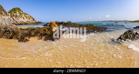 Seichtes Wasser bedeckt den Sand und die Felsen des Mayto Beach in Mexiko. Stockfoto