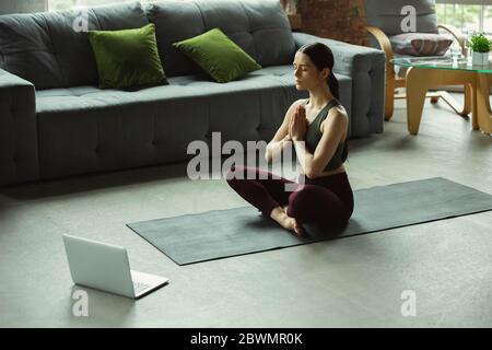 Balance. Sportlich schöne junge Frau, die professionelle Yoga-Unterricht online und üben zu Hause. Konzept des gesunden Lebensstils, Wellness, Wohlbefinden, auf der Suche nach neuen Hobby. Flexibel und motiviert. Stockfoto