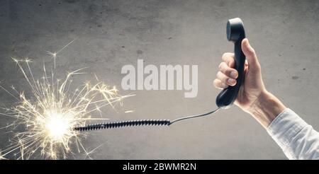 Geschäftsmann hält ein Telefonhörer mit einem brennenden Telefonkabel. Konzept für Notrufhilfe oder Hotline. Stockfoto