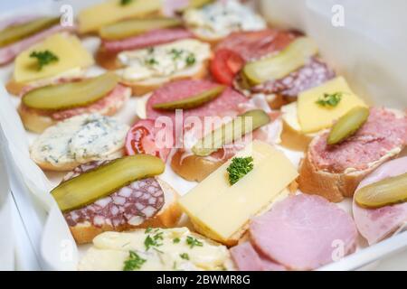 Baguette-Kanapees mit Käse, Schinken und Wurst, garnieren aus Tomaten, Gurken und Kräutern für eine lässige Party, ausgewählte Fokussierung, schmale Schärfentiefe Stockfoto