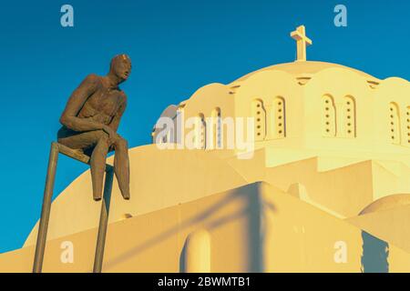 Eine moderne Skulptur gegen die orthodoxe Metropolitan Kathedrale in Thira, Santorin, mit dem goldenen Glanz des Sonnenuntergangs Stockfoto