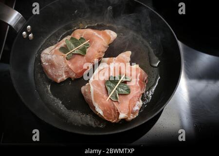 Hähnchen Saltimbocca mit luftgetrockneten Schinken und Salbeiblättern verpackt werden in einer schwarzen Pfanne auf dem Herd gebraten, Kopierraum, ausgewählten Fokus, enge Tiefe des Fi Stockfoto