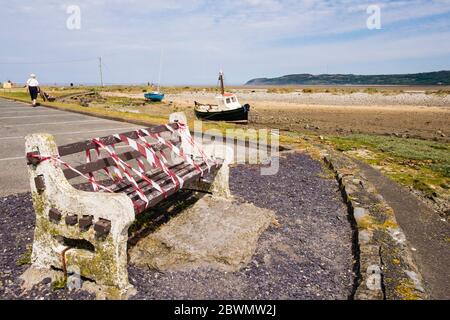 Geschlossene Bank mit rot-weißem Warnband für soziale Distanzierungsregeln während der neuen Covid-19-Sperre im Juni 2020 abgeklebt. Anglesey, Nordwales, Großbritannien Stockfoto