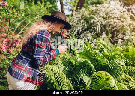 Junge Frau, die im Sommergarten mit Kompaktkamera fotografiert. Glückliches Mädchen, das Bilder von Farn macht Stockfoto