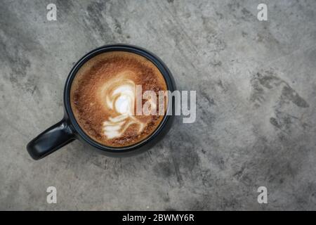 Eine Tasse Kaffee mit Latte Art auf der Oberseite in schwarzem Becher auf grauem Betongrund, Draufsicht Stockfoto