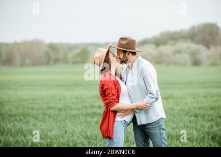 Porträt einer schwangeren Frau mit ihrem Freund, der lässig gekleidet ist und Hüte auf dem Grünfeld zusammen stehen. Glückliches Paar erwartet ein Baby, junge Familie Konzept Stockfoto