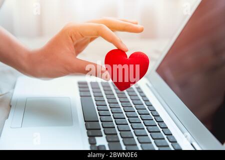 Mädchen Hand nehmen rote Herz am Laptop-Tastatur für soziale Online-Liebe Chat und Austausch Ermutigung über das Internet zu Covid-19 Virus gemeinsam zu bekämpfen. Stockfoto