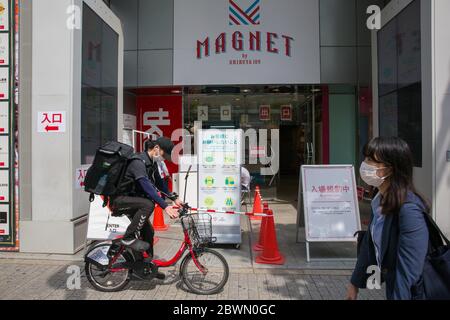 Ein Radfahrer fährt an einem MAGNETEN von SHIBUYA109 Store vorbei, während er eine Gesichtsmaske als vorbeugende Maßnahme beim Anheben des Notfalls trägt. Japan hat den Ausnahmezustand aufgehoben, der 39 von 47 Präfekturen aufgrund des Coronavirus verhängt wurde, nachdem die neuen Infektionen stark zurückgefallen waren. Stockfoto