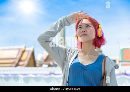 Asiatische Mädchen teen rote Haare gefärbt stehen im Freien gegen hohe UV-Sonne Licht im Sommer Saison sonnigen Tag Himmel Thai Tempel Hintergrund. Stockfoto