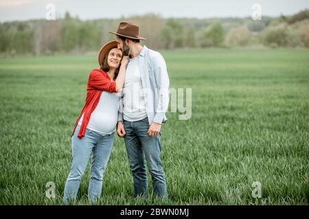 Porträt eines schönen Paares, das zusammen auf dem grünen Feld steht. Glückliches Paar erwartet ein Baby, junge Familie Konzept Stockfoto