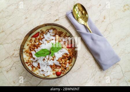 Smoothie Schüssel mit Mango, Joghurt, Müsli und Erdbeere in Kokosnussschale Schüssel auf hellem Hintergrund, Draufsicht Stockfoto