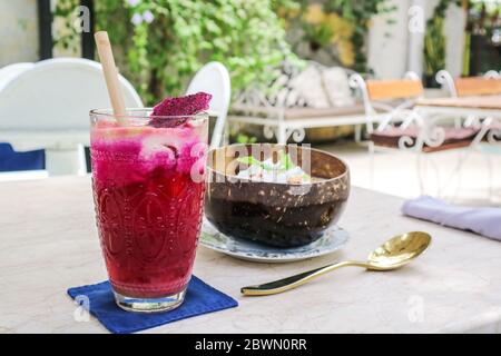 Rosa Saft mit Äpfeln, Rote Bete, Drachenfrucht und Limette im Glas mit Bambus Trinkhalm und Smoothie Schüssel auf dem Tisch im Café Stockfoto