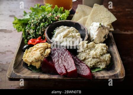 Mezze Platte mit Hummus, Babaganoush, Tabouli, gerösteten Paprika, Rüben, Feta-Käse und kalamata Oliven serviert mit Pita-Brot auf Holzhintergrund, c Stockfoto