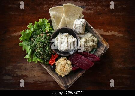 Mezze Platte mit Hummus, Babaganoush, Tabouli, gerösteten Paprika, Rüben, Feta-Käse und kalamata Oliven serviert mit Pita-Brot auf Holzhintergrund, t Stockfoto