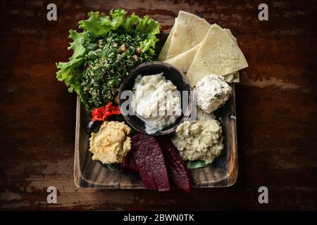 Mezze Platte mit Hummus, Babaganoush, Tabouli, gerösteten Paprika, Rüben, Feta-Käse und kalamata Oliven serviert mit Pita-Brot auf Holzhintergrund, t Stockfoto