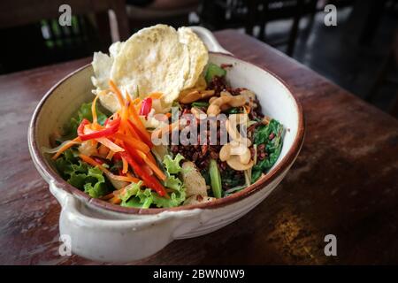 Bio-Reis Nasi Goreng, vegetarischer gebratener Reis mit viel Gemüse, Tofu & gerösteten Cashewkernen in einer Schüssel auf Holzhintergrund Stockfoto