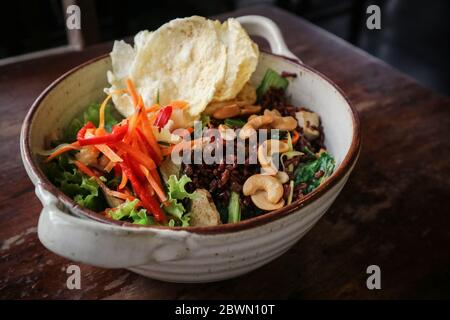 Bio-Reis Nasi Goreng, vegetarischer gebratener Reis mit viel Gemüse, Tofu & gerösteten Cashewkernen in einer Schüssel auf Holzhintergrund Stockfoto