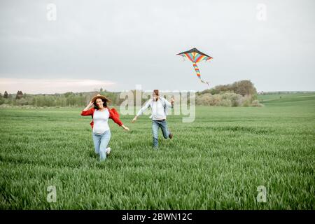 Glückliches Paar, das Spaß zusammen hat, mit Drachen auf dem Greenfield spielt. Glückliches Paar erwartet ein Baby und junge Familie Konzept Stockfoto