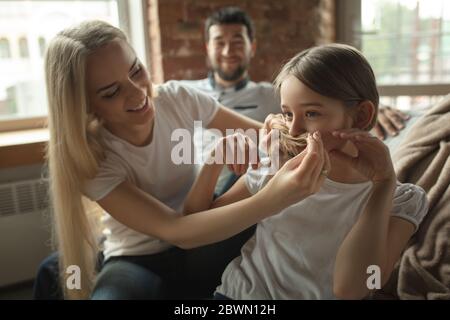 Mutter, Vater und Tochter zu Hause mit Spaß, Komfort und gemütliche Konzept. Sieht glücklich, fröhlich und fröhlich aus. Wunderschöne kaukasische Familie. Zeit zusammen verbringen, eine Frisur machen, Scrollen Tablet. Stockfoto