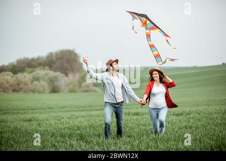 Glückliches Paar, das Spaß zusammen hat, mit Drachen auf dem Greenfield spielt. Glückliches Paar erwartet ein Baby und junge Familie Konzept Stockfoto