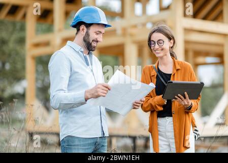 Bauherrin mit einer Kundin in der Nähe der Holzhausstruktur auf der Baustelle im Freien. Bau und Gestaltung Holzrahmenhaus Konzept Stockfoto