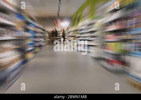 Einkaufen im Supermarkt während der Coronavirus-Krise Ausgangssperre, wenige Menschen zwischen vollen Regalen, Zoom-Bewegung verschwimmen Stockfoto