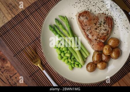 Gegrilltes Thunfischsteak mit Spargel, gebratenen Babykartoffeln, Edamamebohnen und Sauce Hollandaise auf einem Teller, Draufsicht Stockfoto