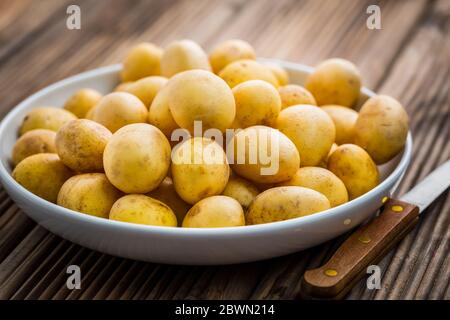 Frische Bio-Kartoffeln in Schüssel mit Messer auf Holzhintergrund Stockfoto