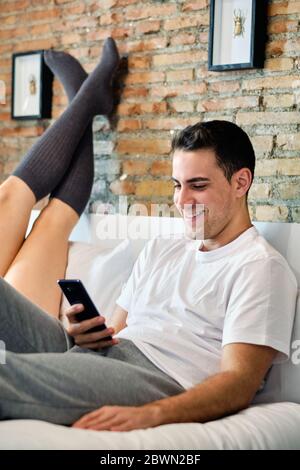 Junger Mann, der zu Hause auf dem Bett auf das Handy schaut Stockfoto