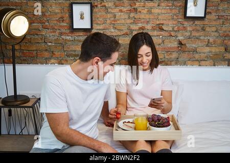 Junges Paar mit Frühstück und Entspannung auf dem Bett im Haus. Stockfoto