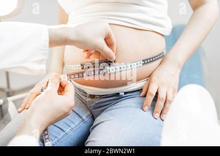 Arzt Messung der Bauch schwangere Frau mit einem Band während einer medizinischen Untersuchung, beschnitten Ansicht ohne Gesicht auf den Bauch konzentriert Stockfoto