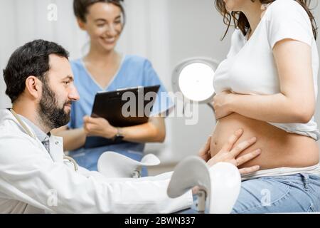 Männlicher Arzt mit einer Krankenschwester während einer ärztlichen Untersuchung einer schwangeren Frau im Büro. Konzept der medizinischen Versorgung und Gesundheit während einer Schwangerschaft Stockfoto