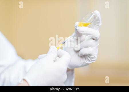 Arzt, der Impfstoff oder Medikamente in einer Spritze pflückt, Nahaufnahme, die auf die Hände auf dem gelben Hintergrund gerichtet ist Stockfoto