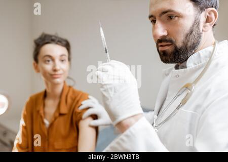 Arzt hält Impfstoff oder einige Medikamente in der Spritze, Vorbereitung für die Injektion für eine junge Frau während eines medizinischen Verfahrens in der Klinik Stockfoto