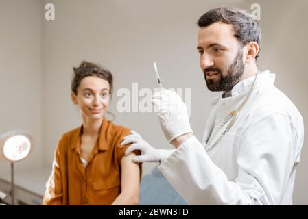 Arzt hält Impfstoff oder einige Medikamente in der Spritze, Vorbereitung für die Injektion für eine junge Frau während eines medizinischen Verfahrens in der Klinik Stockfoto