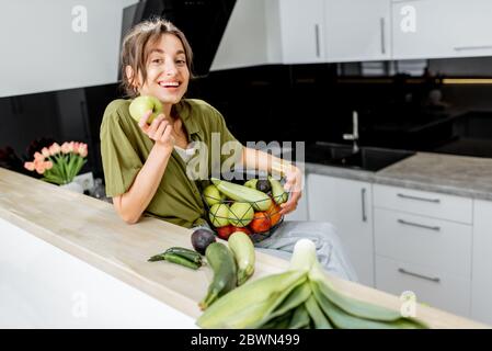 Porträt einer jungen und fröhlichen Frau mit gesundem Rohkost in der Küche zu Hause. Vegetarismus, Wohlbefinden und gesundes Lifestyle-Konzept Stockfoto