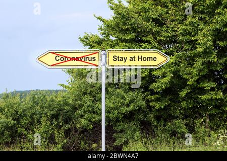 Gelbe Straßenschilder zeigen in entgegengesetzte Richtungen mit Text Coronavirus und Aufenthalt zu Hause, ländliche Landschaft im Hintergrund, Gesundheitskonzept durin Stockfoto